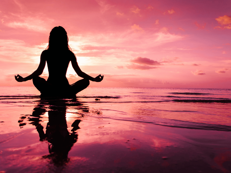 silhouette of woman sitting above water and meditating against the background of pink skies