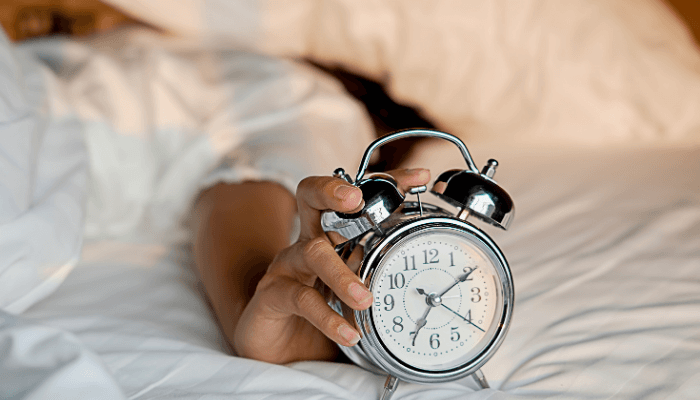women trying to stop alarm clock with her hand while in bed