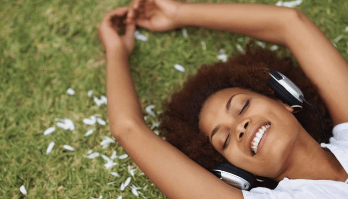 woman listening to music while lying in grass field