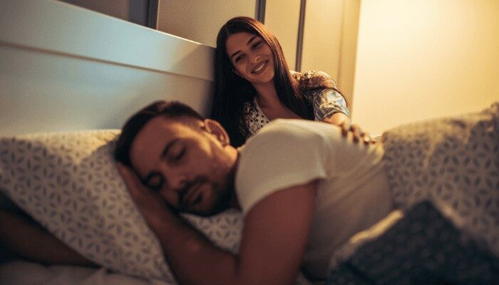 women smiling beside sleeping person in bed