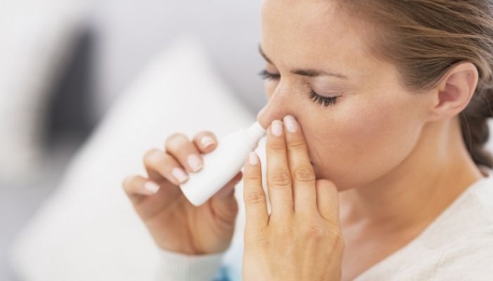 woman spraying medicine inside nose