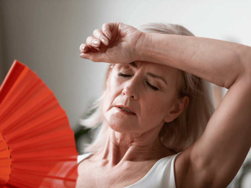 woman fanning herself due to hot flashes, a common menopausal symptom 