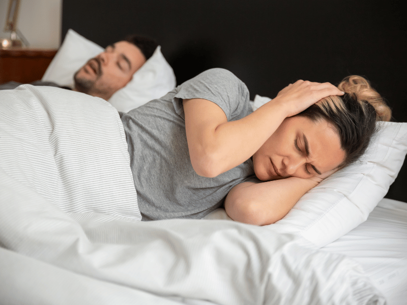 woman covering ears due to partner snoring in bed