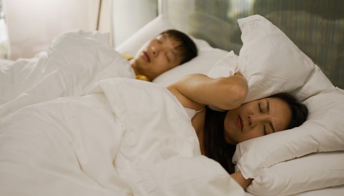 woman holding pillow in her ear while sleeping beside a male person