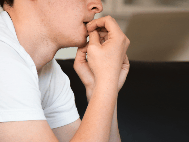 A tired man rests on a couch, biting his nail, showing signs of anxiety from lack of sleep