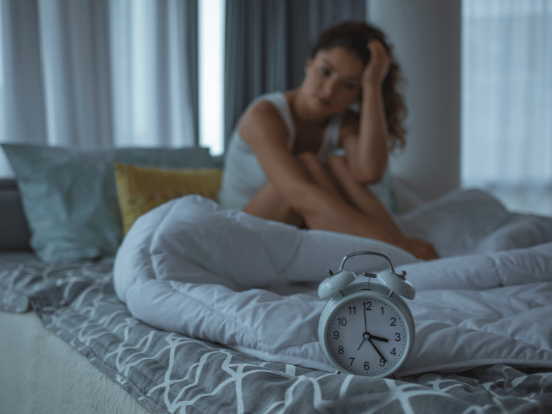 a woman struggling with insomnia and not able to get deep sleep, on the bed and holding her head