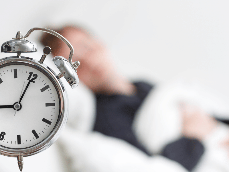 A man peacefully sleeps in bed, with an alarm clock nearby, following the Uberman sleep cycle.