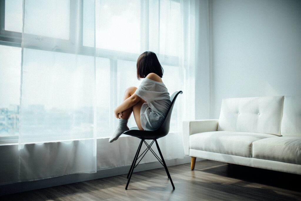 woman sitting on black chair in front of glass-panel window with white curtains
