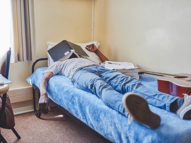 man sleeping on bed with book covering face how much sleep is too much?