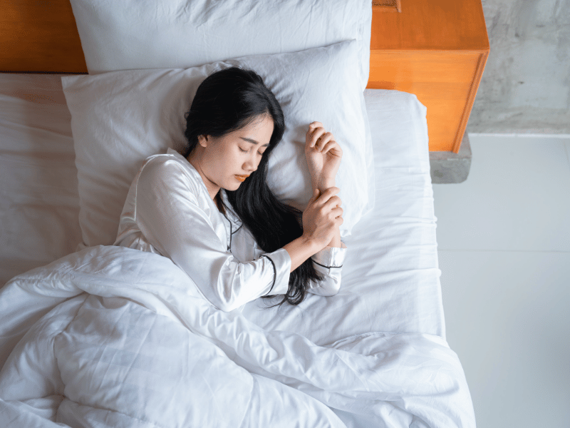 A woman peacefully sleeping in a cozy bed with soft white sheets surrounding her.