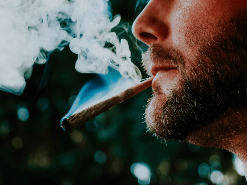 close up of a bearded man with a weed joint in his mouth and smoking away