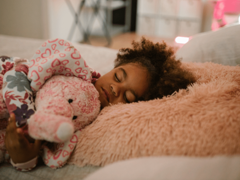 a young girl sleeping on the bed hugging a soft toy with her head towards the east direction