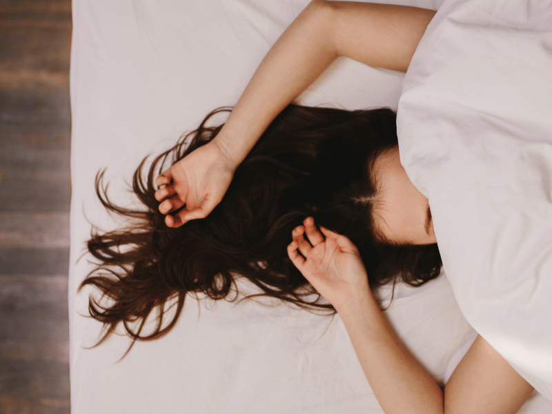 woman sleeping, covering her face with her blanket and her head pointed towards the west direction