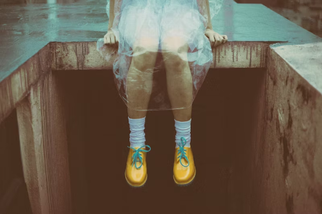 Person wearing a translucent raincoat, white socks, and yellow shoes with blue laces, sitting on a concrete ledge: Shoes dream meaning