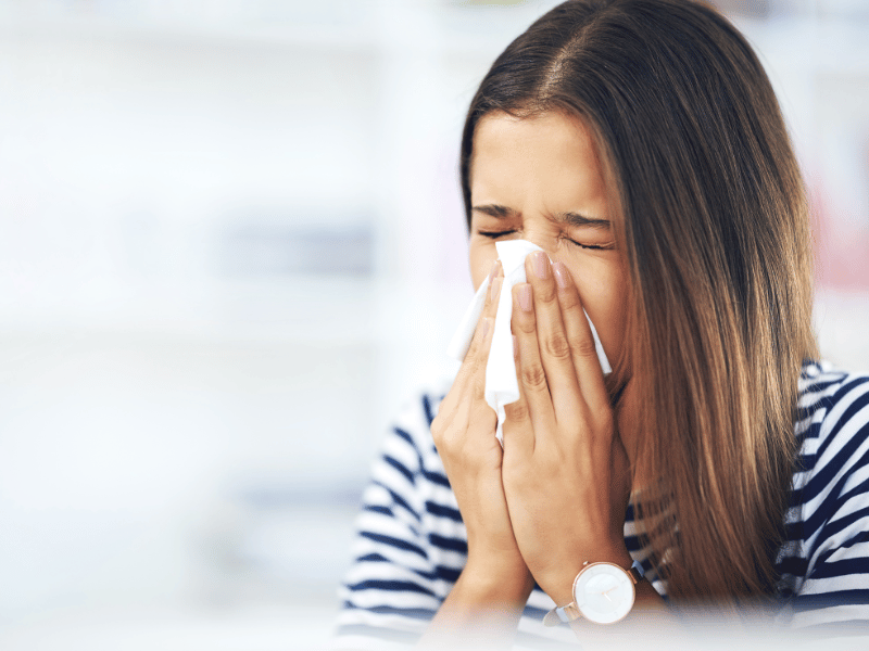 woman blowing her nose and having sore throat from allergies