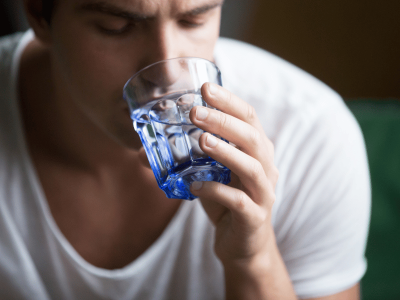 man drinking water from a glass as a result of dehydration from snoring