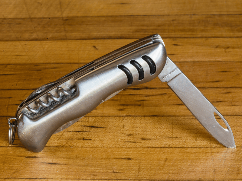 a silver pocket knife placed upright on top of a wooden surface