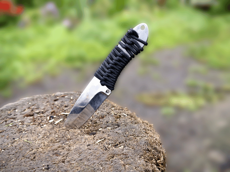 a thrown knife with black lace wrapped around the handle and wedged into the ground