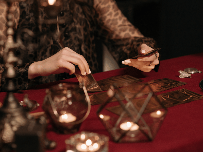 woman holding tarot cards in her hand and sitting in front of red clothed table with other tarot cards