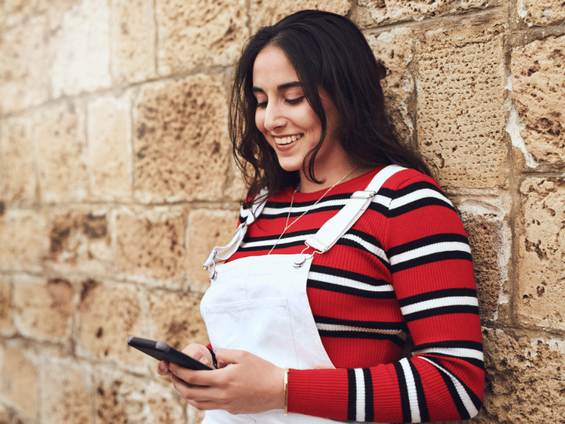 girl smiling and looking down at her phone, seeing a celebrity crush