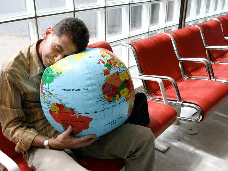 man sleeping on a world map cushion in the airport, suffering from jet lag symptoms