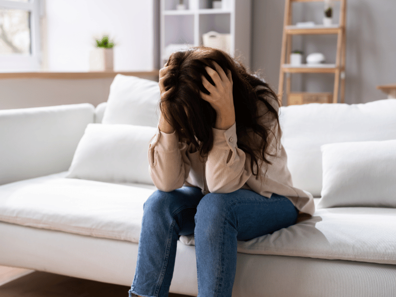 woman holding her head in frustration while sitting on couch as a result of mood disorders