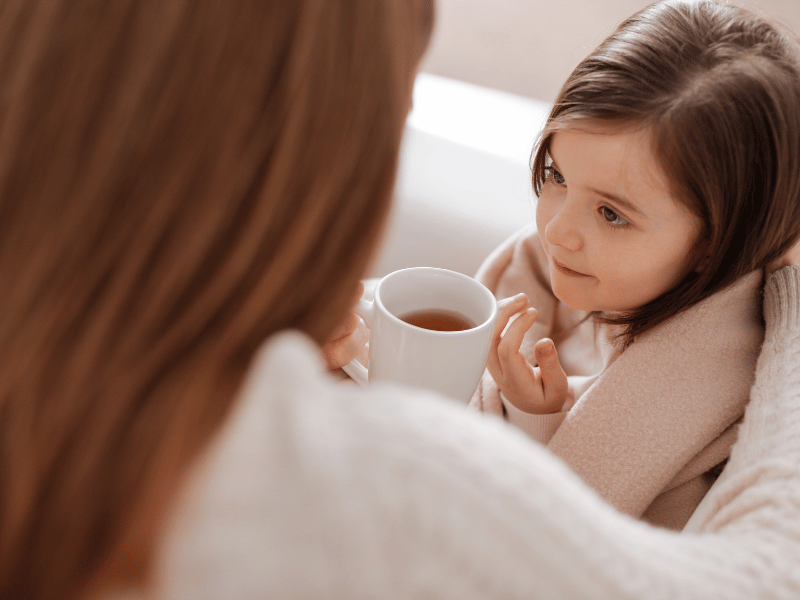 mum handing a cup of warm tea to her child who is recovering from a cold