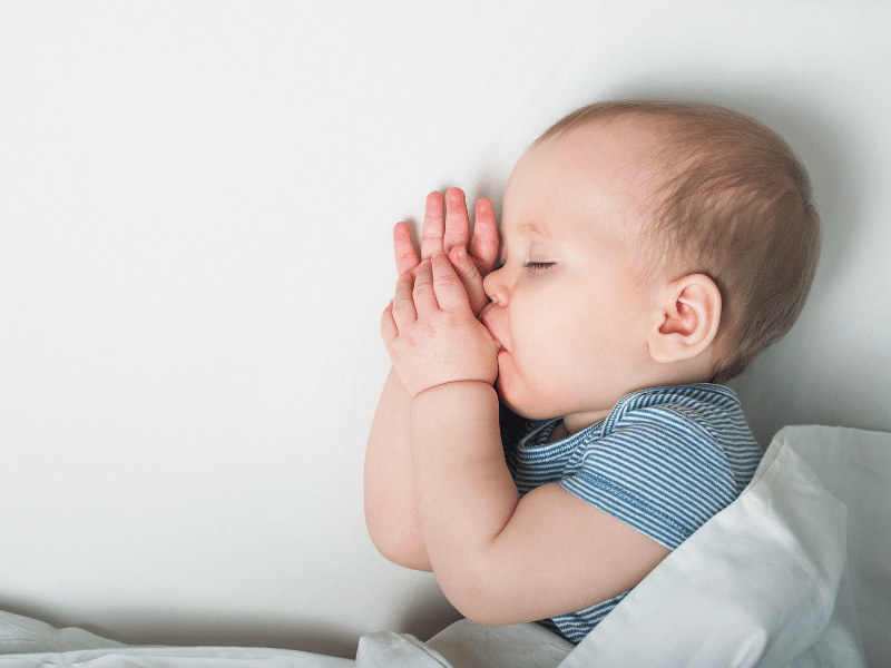 baby sucking on thumb with eyes closed, sleep training beneficial for reducing infant sleep problem