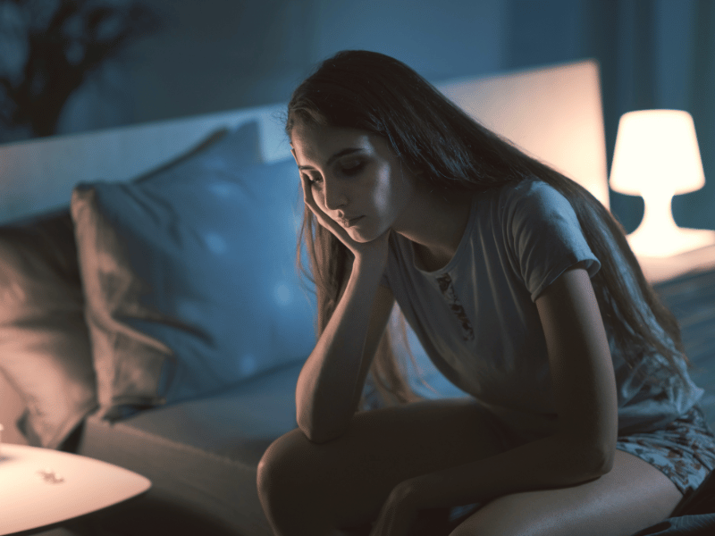 woman sitting on her bed and looking stressed and unable to sleep at night