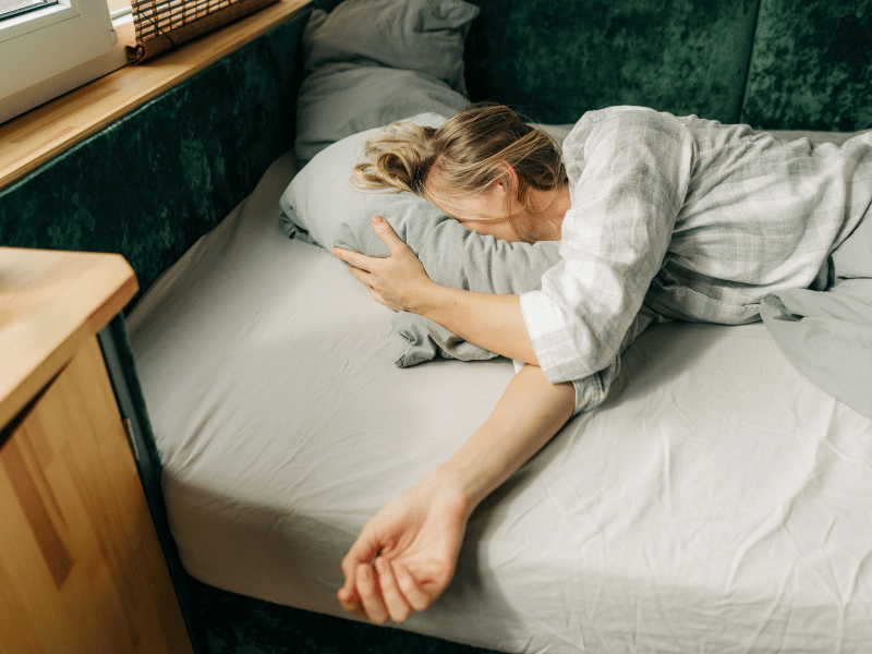 A woman peacefully getting more rest in bed, her arm stretched out comfortably beside her.