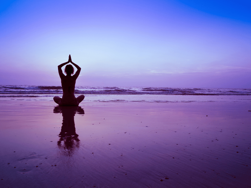 woman sitting on the beach and meditating against a blue and purple sky backdrop for sleep and healing