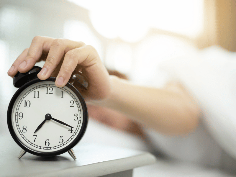 hand on alarm clock representing avoid snoozing 